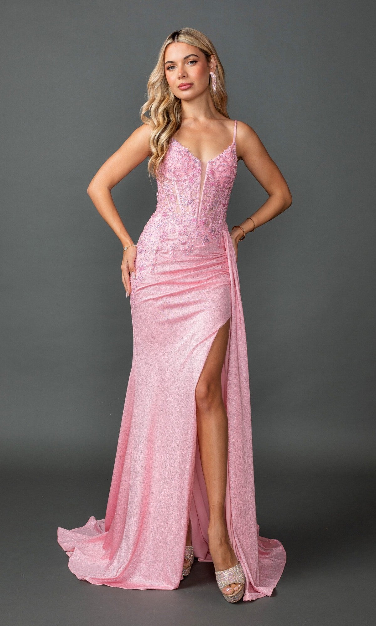 A woman stands against a plain dark background wearing the Beaded-Bodice Pink Prom Gown: Dancing Queen 4556, featuring a corset-style bodice, thigh-high slit, lace details, and spaghetti straps.